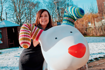 Jane Hogan, poses with giant Snowdog sculpture in a snowy garden